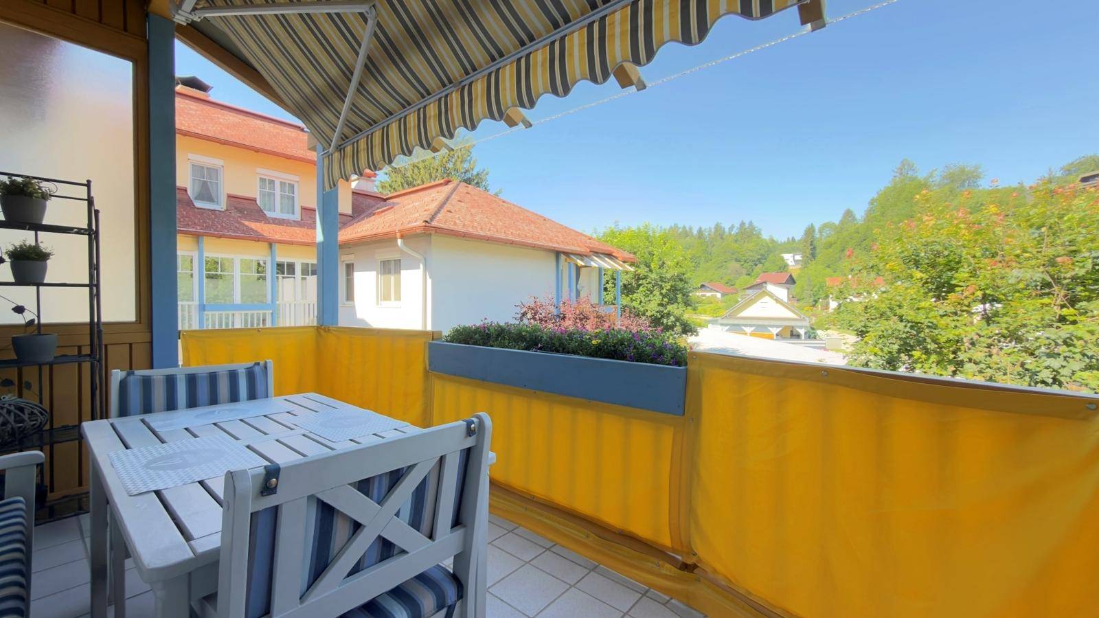 Möblierter Balkon mit Markise, Fliesenboden und Blick auf die Umgebung.