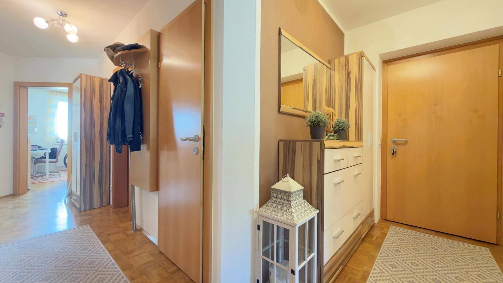 Heller Flur mit Holzmöbeln, Spiegel und Garderobe.