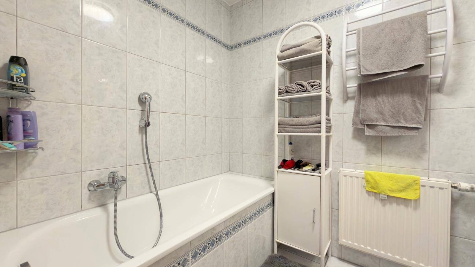Badezimmer mit Badewanne, weißen Fliesen und Handtuchheizkörper.