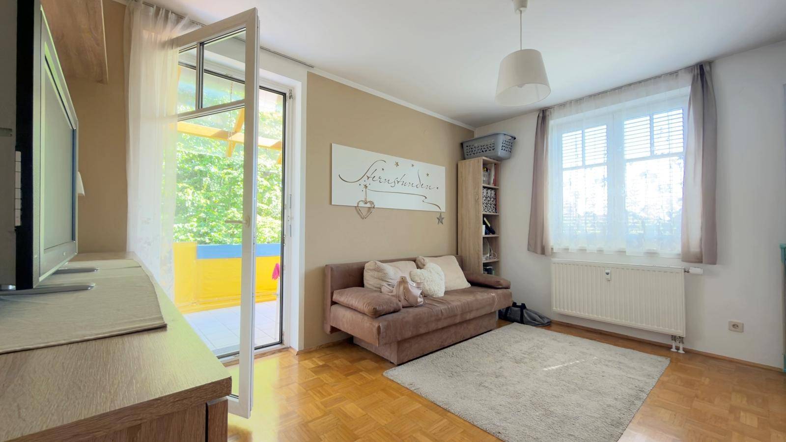 Helles Zimmer mit Schlafsofa, Parkettboden und direktem Zugang zum Balkon.