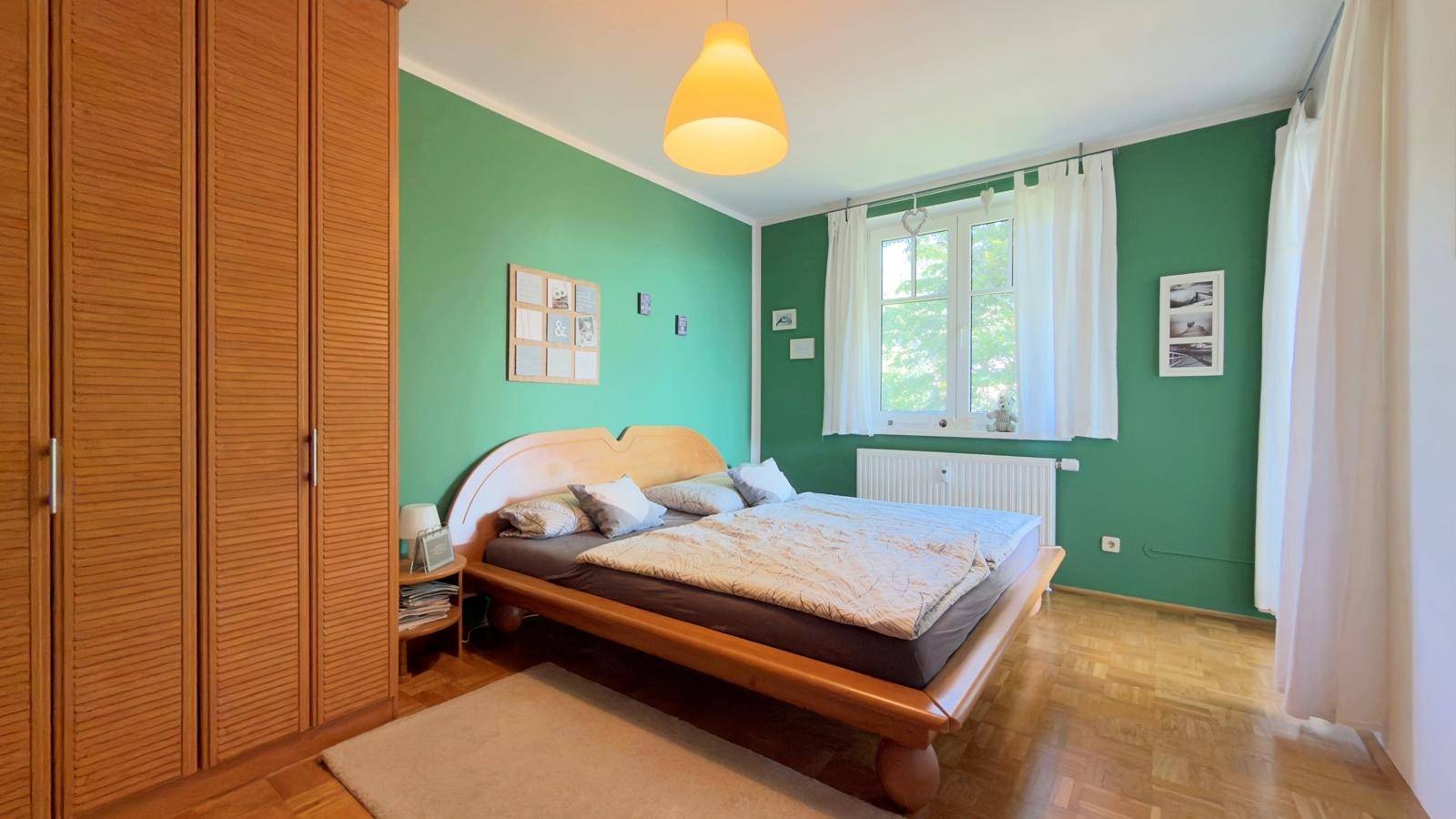 Schlafzimmer mit grünen Wänden, Holzdoppelbett und Parkettboden.