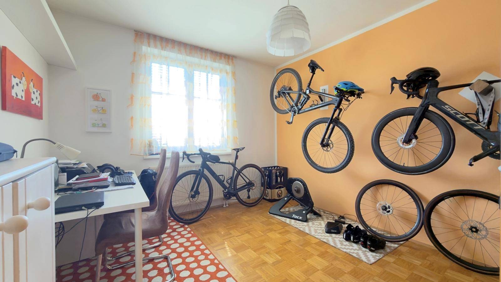 Vielseitiger Raum mit Schreibtisch, Fahrradhalterungen und Parkettboden.