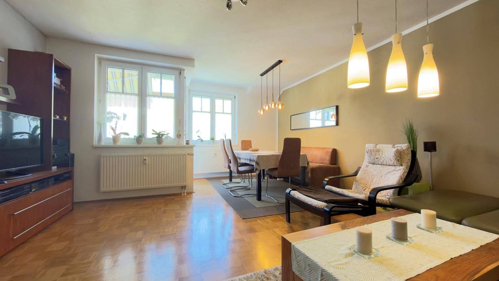 Gemütlicher Wohnbereich mit Parkettboden, großen Fenstern und moderner Beleuchtung.