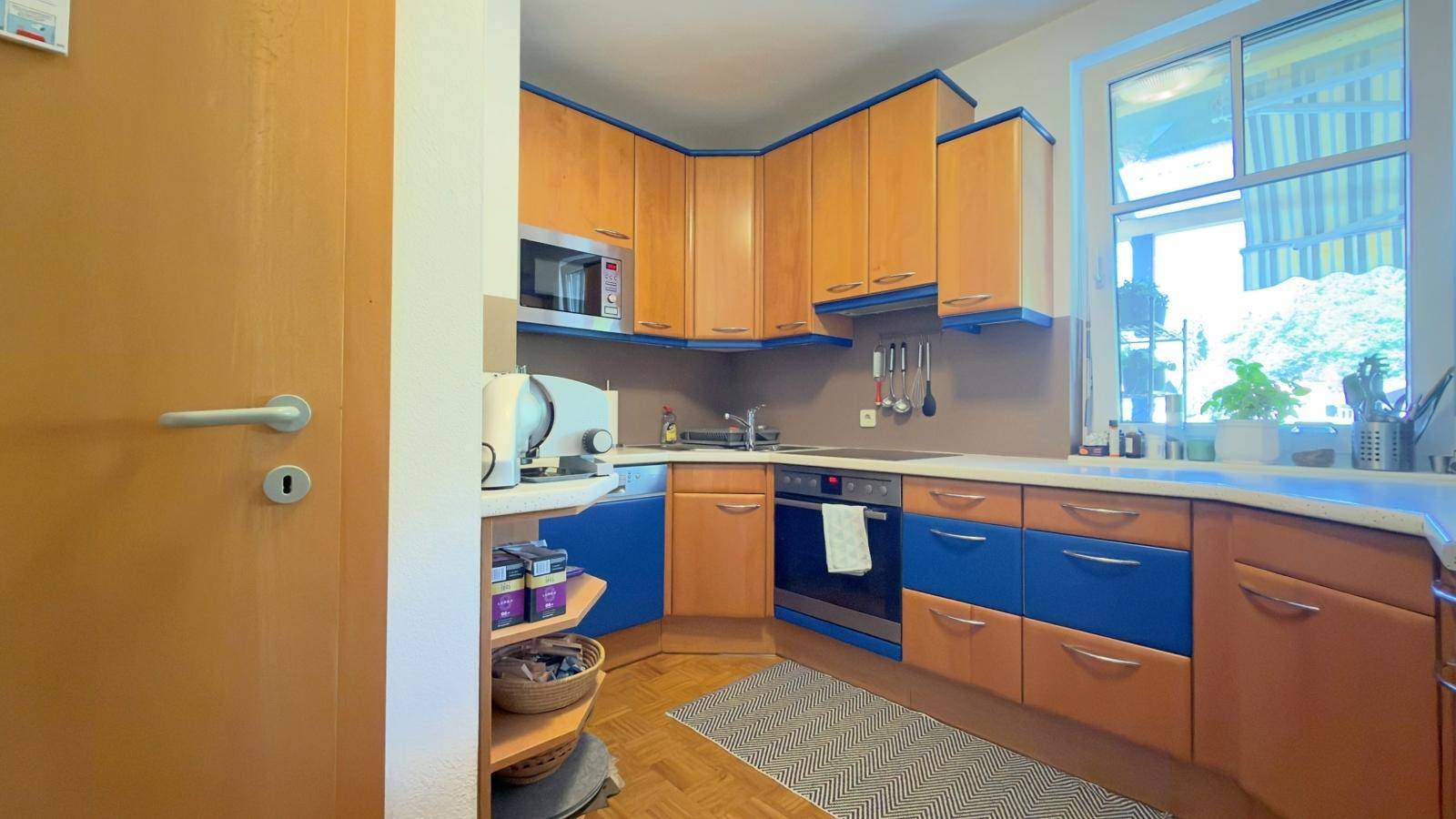 Funktionale Küche mit Holz- und blauen Fronten, Fenster und integrierten Geräten.