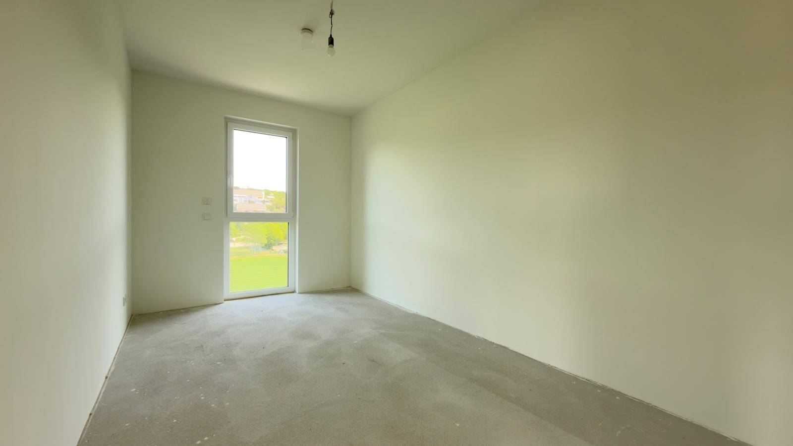 Helles Schlafzimmer im Rohbau mit Betonboden und Fenster zum Außenbereich.