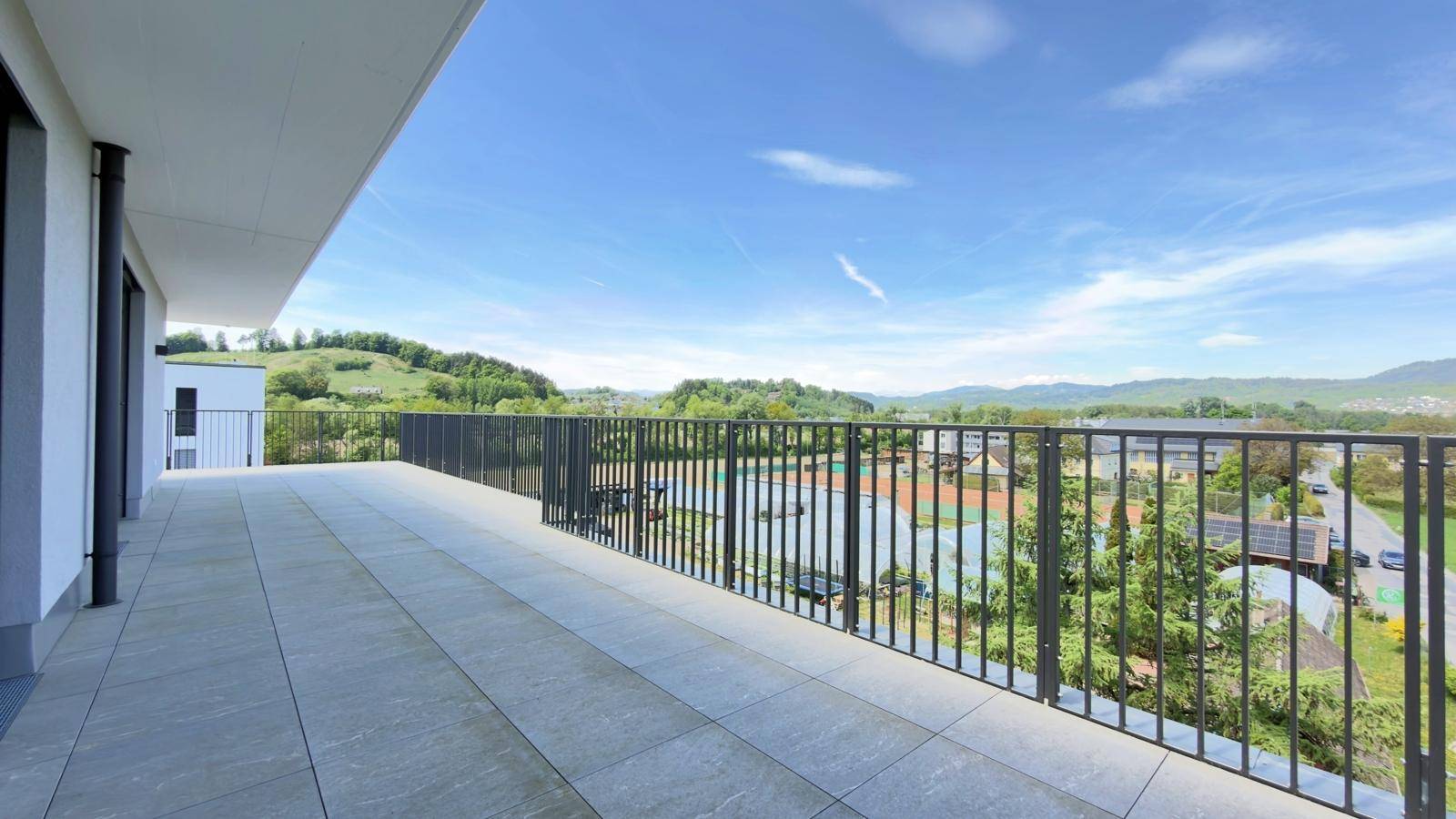 Weitläufige Terrasse mit Metallgeländer und Ausblick auf die grüne Umgebung und Sportanlagen.