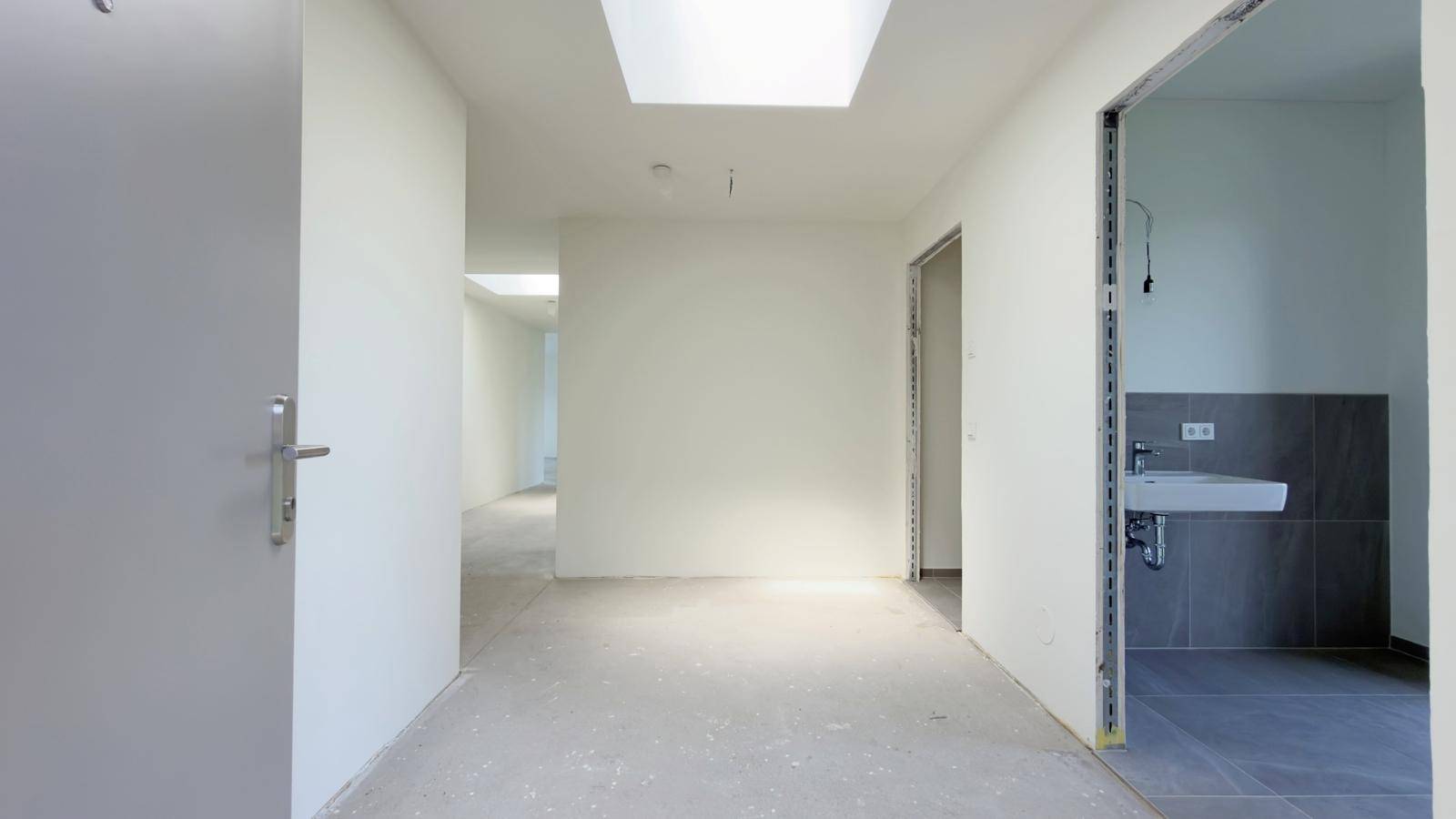 Geräumiger Flur im Rohbau mit Oberlicht und Zugang zu einem Gäste-WC.