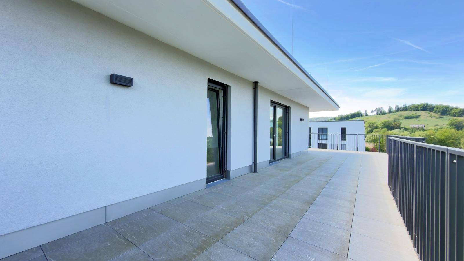 Lange, geflieste Terrasse entlang der Fassade mit Zugang zu den Innenräumen.