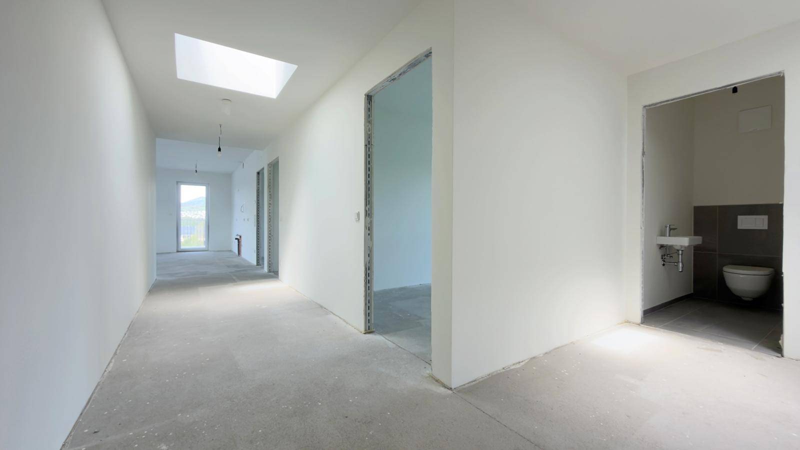 Heller Flur im Rohbau mit Betonboden, Oberlicht und Zugängen zu weiteren Räumen.