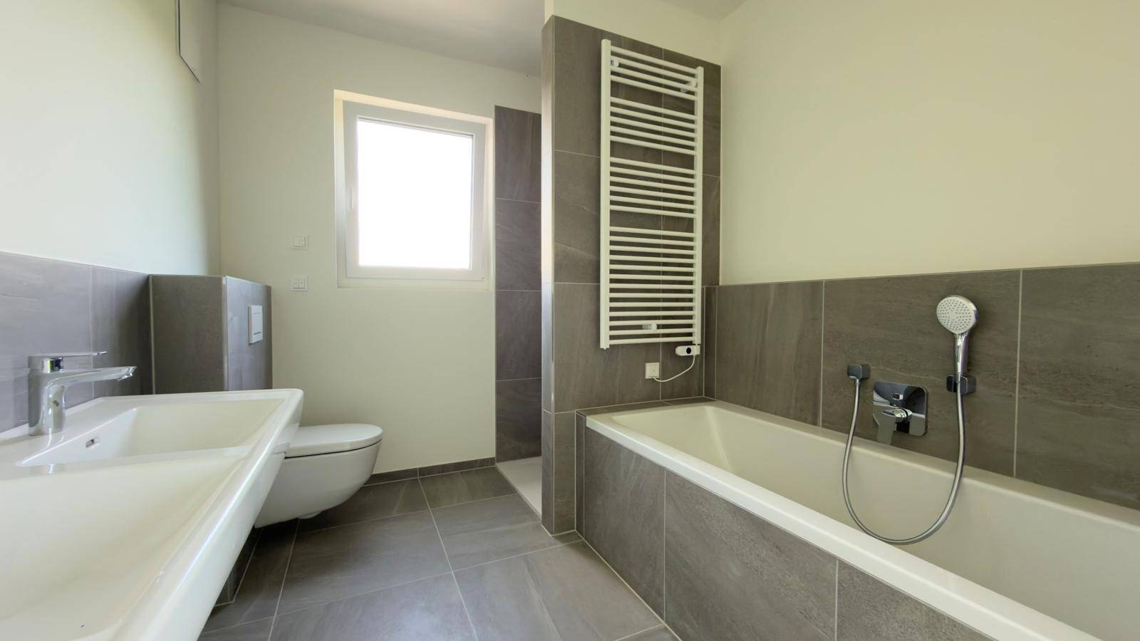 Modernes Badezimmer mit Badewanne, Dusche, WC, Waschbecken und beheiztem Handtuchhalter.