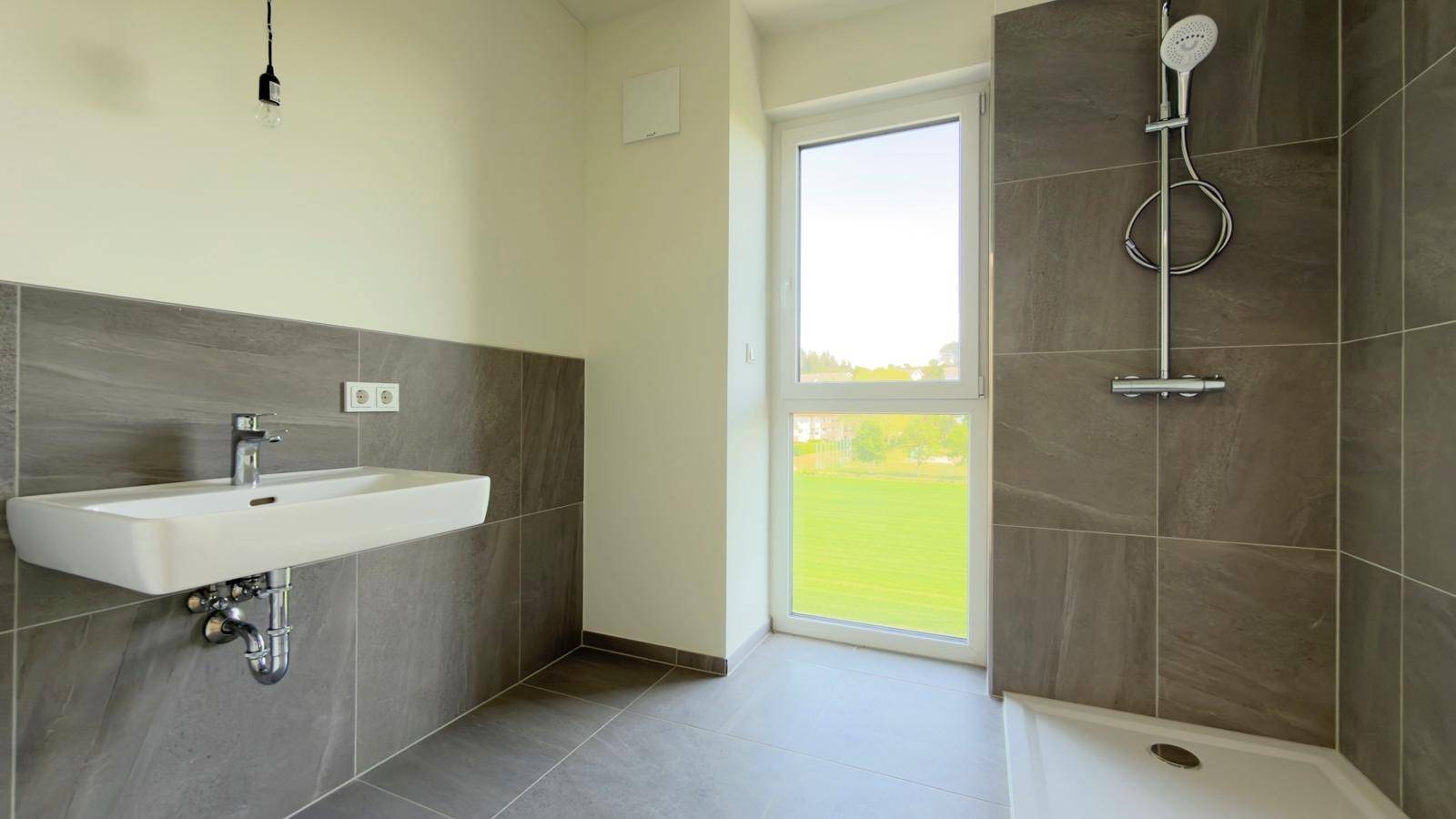 Modernes Badezimmer mit Dusche, Waschbecken und Fenster, teilweise gefliest.