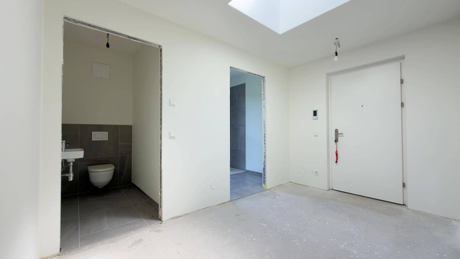 Eingangsbereich im Rohbau mit Betonboden, Oberlicht und Zugang zum Gäste-WC.