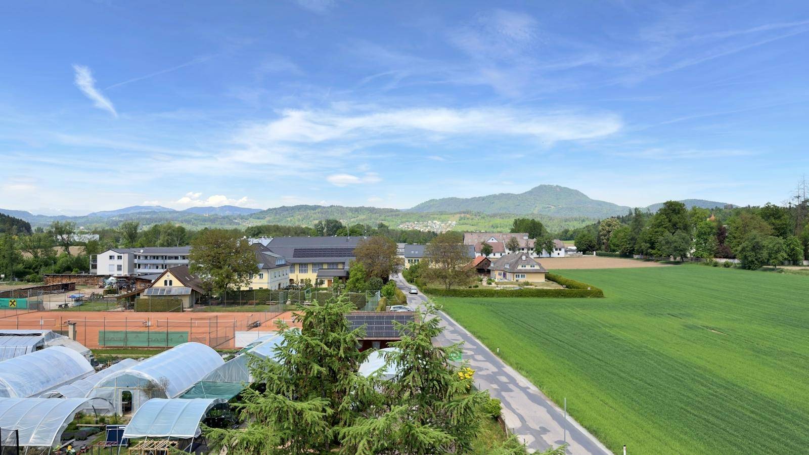 Panoramablick über weite grüne Felder, umgeben von ländlicher Bebauung und Bergen.