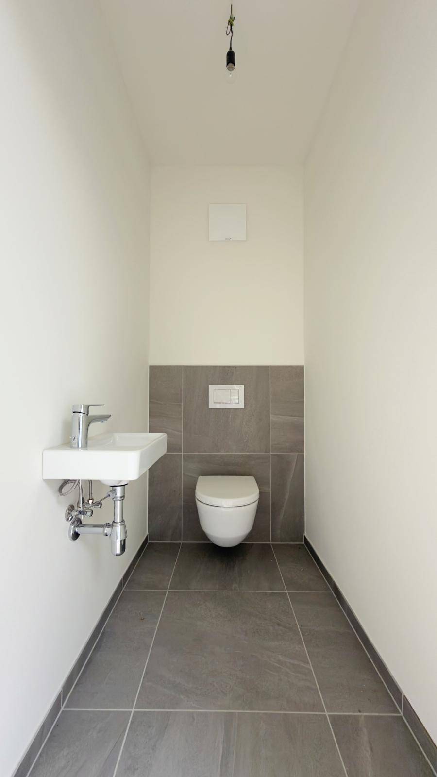 Modernes Gäste-WC mit Wand-WC und kleinem Waschbecken, teilweise gefliest.