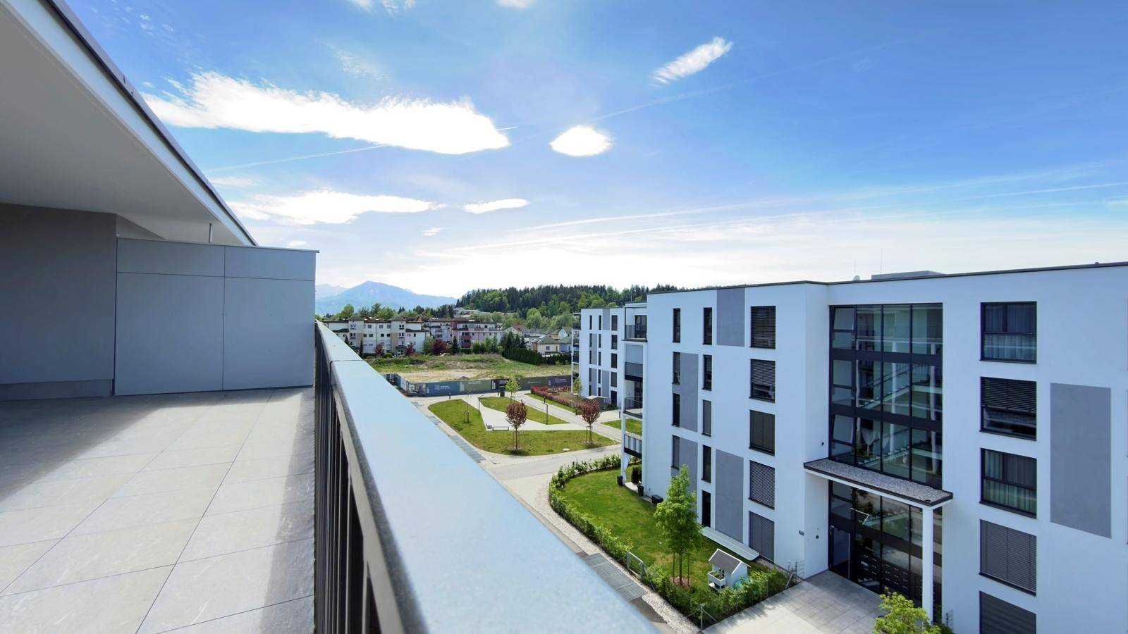 Blick von der Terrasse auf die moderne Wohnanlage und die umliegende Berglandschaft.