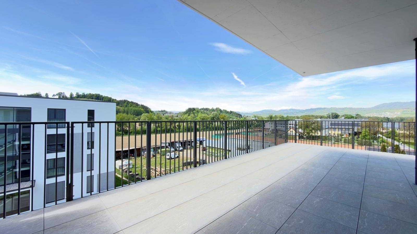 Geräumige Terrasse mit Fliesenboden und weitem Blick über grüne Hügel und Tennisplätze.