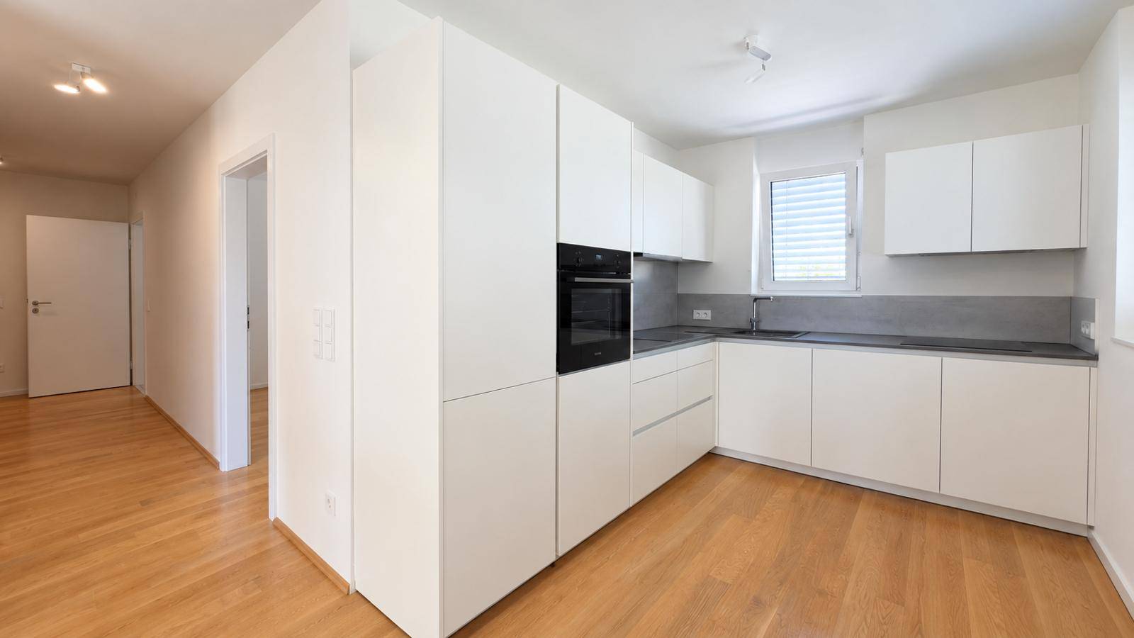Heller, leerer Raum mit Holzboden, großen Fenstern und Zugang zu einem Balkon.