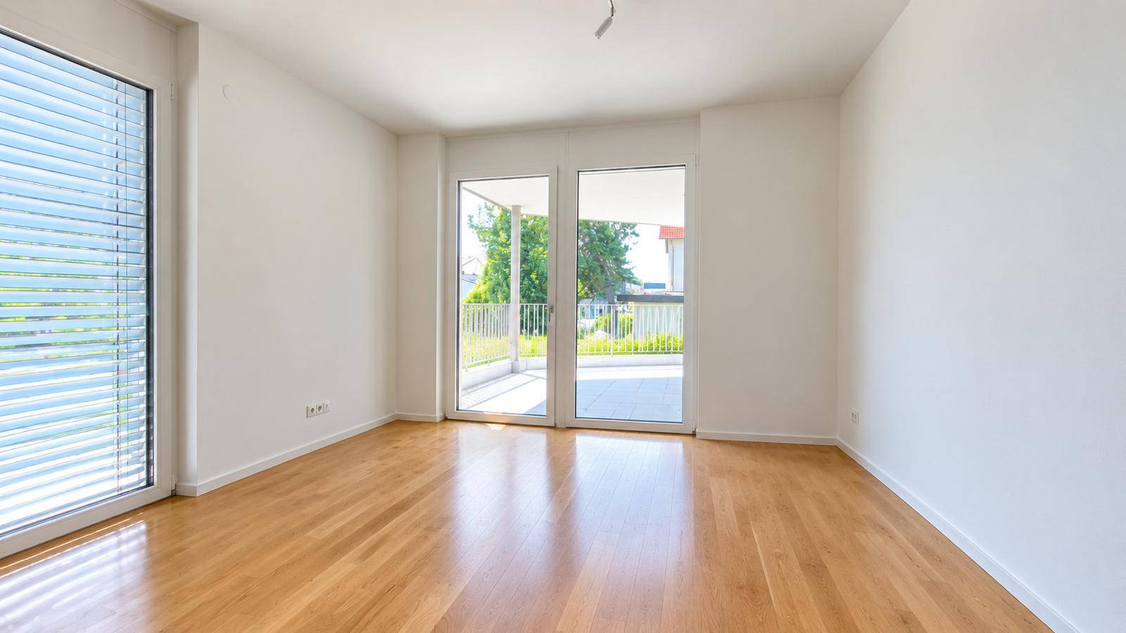 Sonniger Balkon mit Blumenkästen und Blick auf die umliegende Wohngegend und Grünflächen.