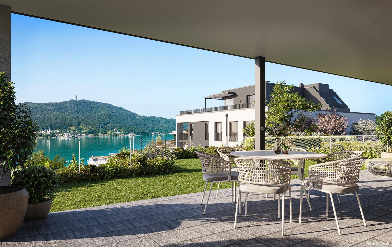 Geräumige Terrasse mit Esstisch und Stühlen, umgeben von Rasen und mit Blick auf den See und die Berge.