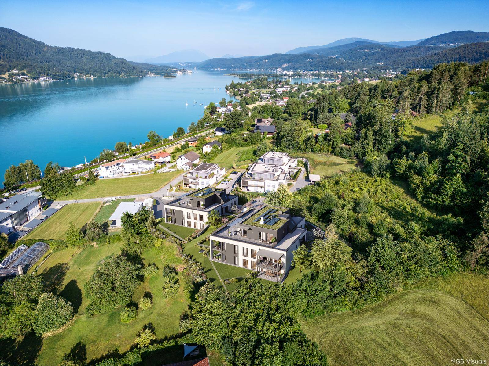 Weitläufige Luftaufnahme von modernen Wohnanlagen am Seeufer, umgeben von üppiger Natur und Bergen.