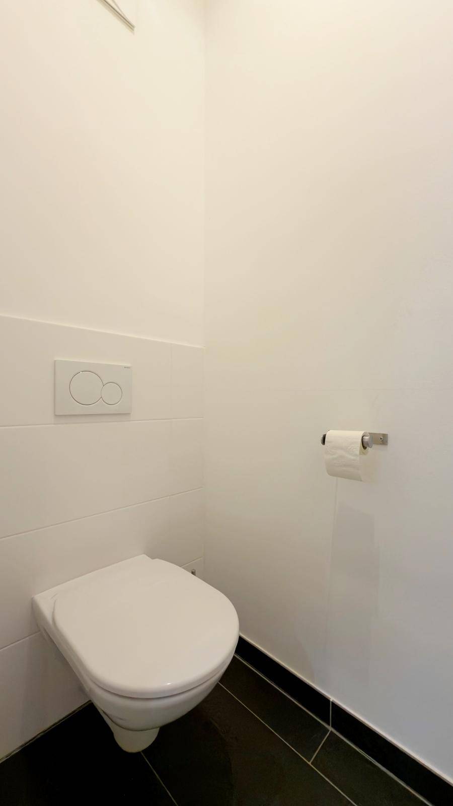 Saubere Gästetoilette mit wandhängendem WC und dunklen Bodenfliesen in modernem Design.