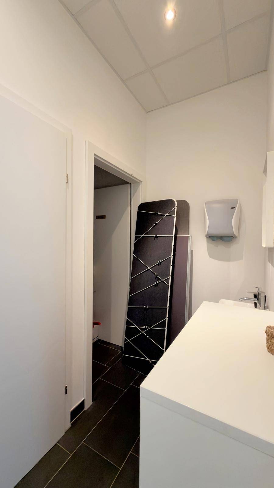 Kleiner Flur führt zu einer Gästetoilette mit Waschbecken und dunklen Bodenfliesen.