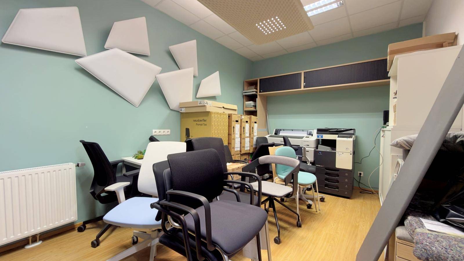 Bürobereich mit verschiedenen Bürostühlen, einem Drucker und schallabsorbierenden Paneelen an der Wand.