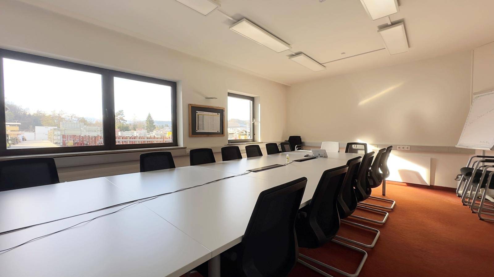 Heller Konferenzraum mit langem Tisch, bequemen Bürostühlen und Fenstern, die viel Tageslicht hereinlassen.