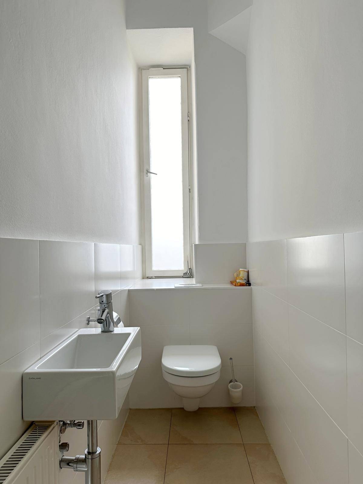 Kleines Gäste-WC mit wandhängender Toilette, Waschbecken und hohem Fenster.