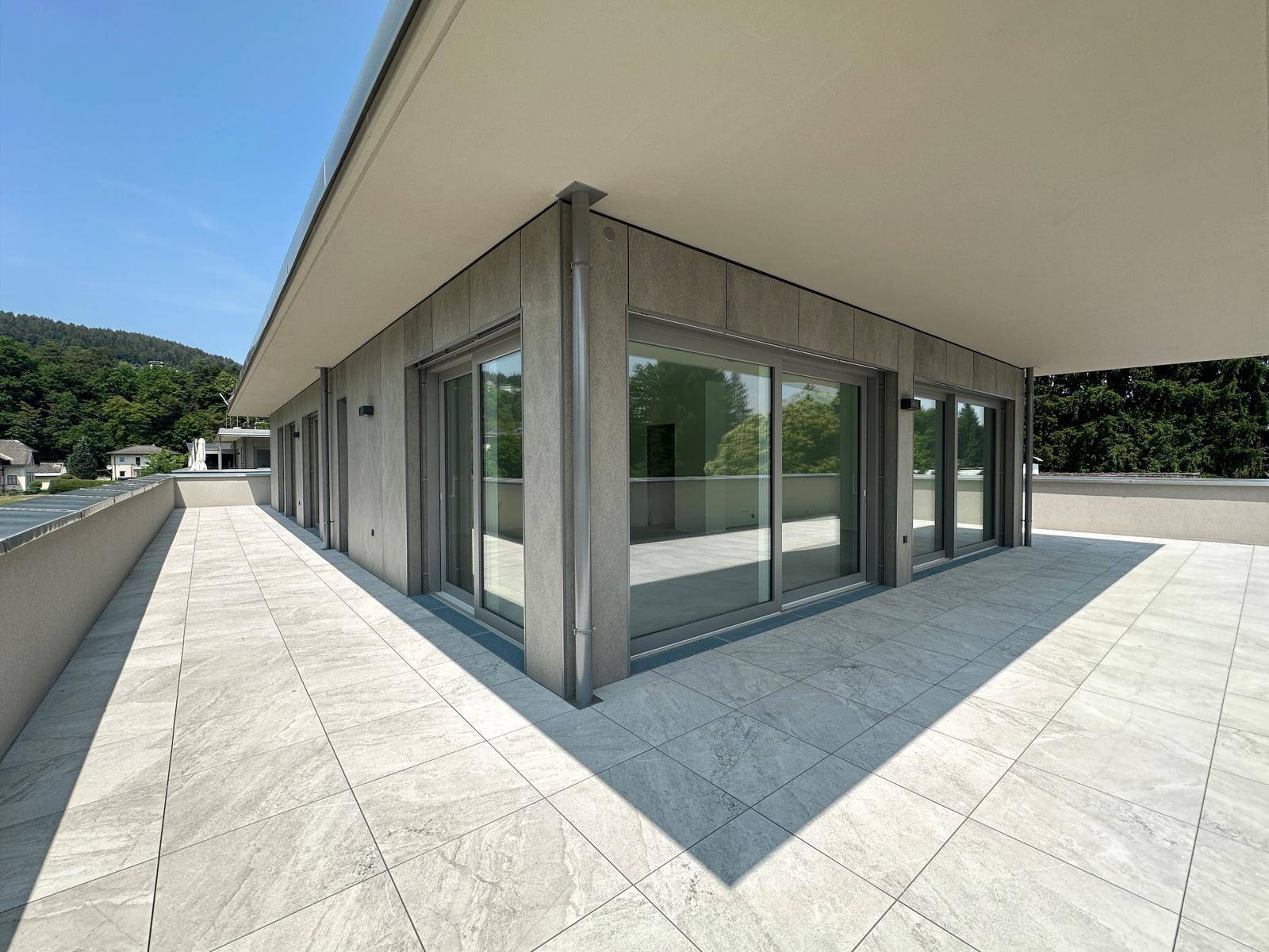 Geräumige, modern geflieste Terrasse mit großen Glasfronten und viel Sonnenlicht.