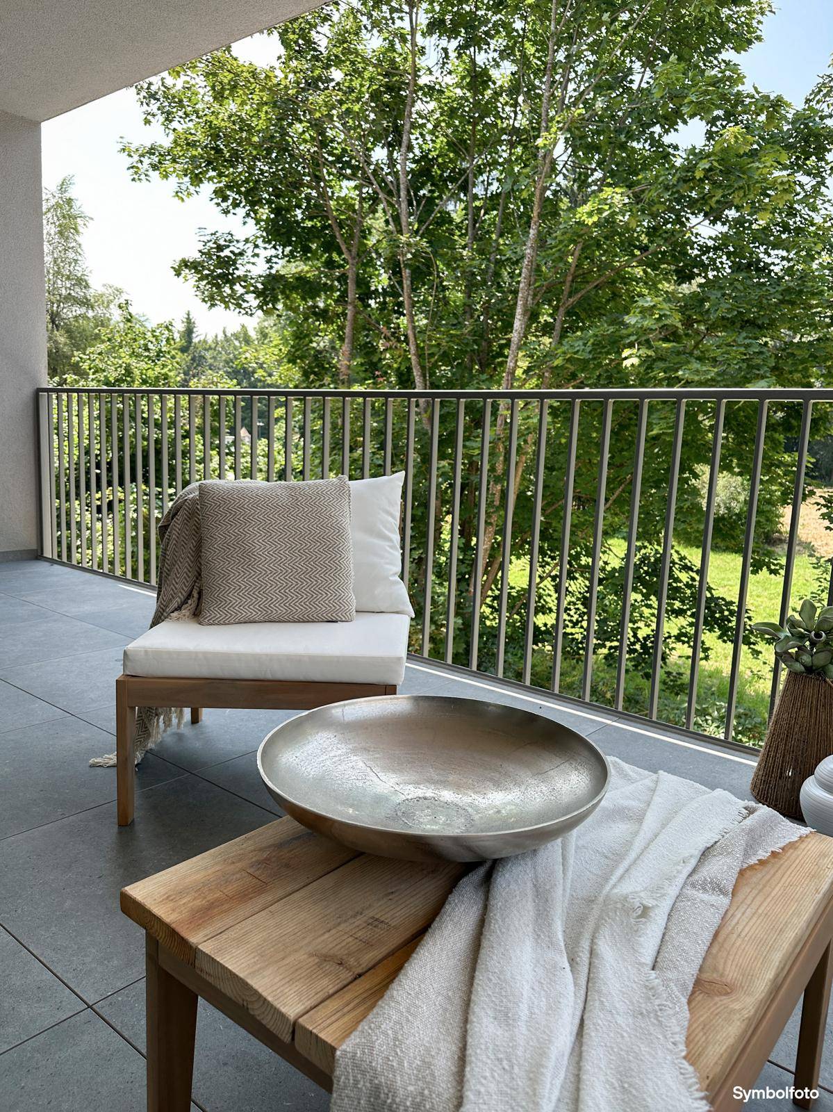 Heller Balkon mit Fliesenboden, Holzstuhl und einem schönen Blick ins Grüne.