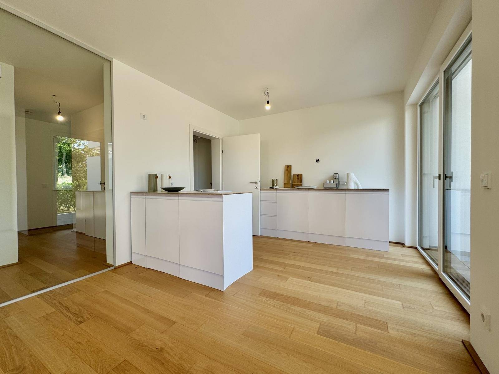 Moderne Küche mit weißen Unterschränken, Holz-Arbeitsplatten und Eichenparkett, hell durch große Fenster.