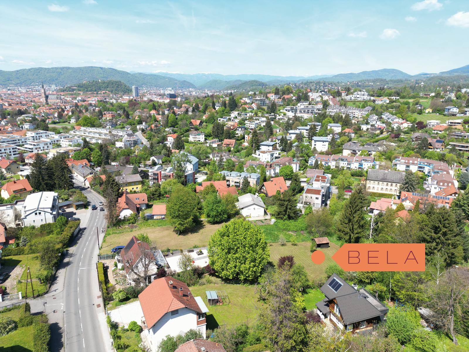 Luftaufnahme einer grünen Wohngegend mit vielen Häusern, Straßen und Bergen im Hintergrund.