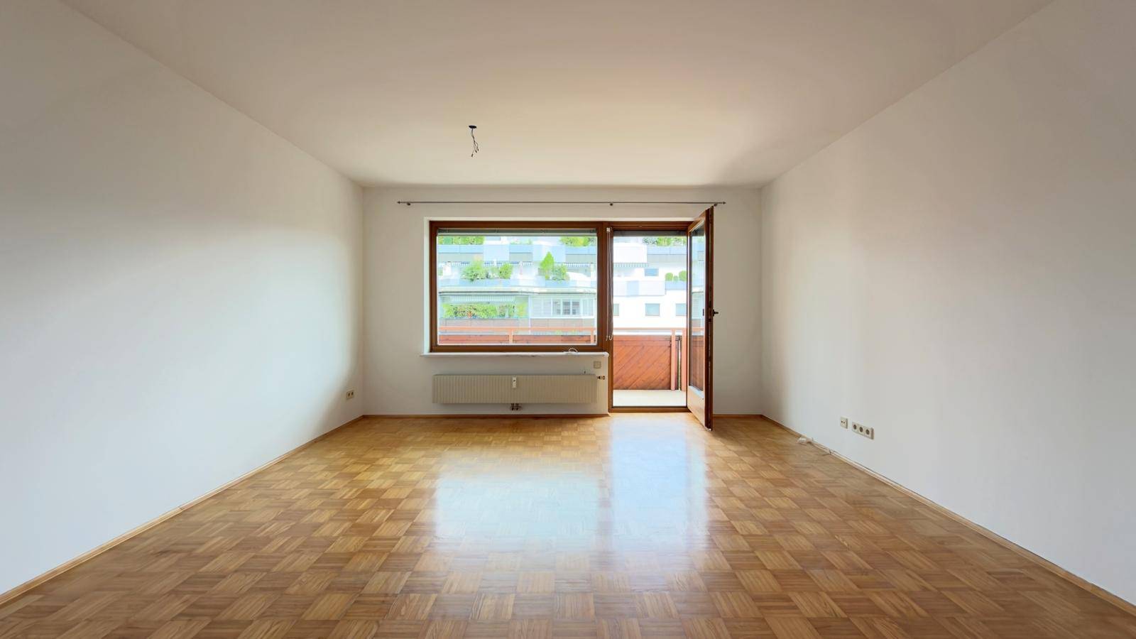 Helles, leeres Wohnzimmer mit Parkettboden und direktem Zugang zum Balkon.