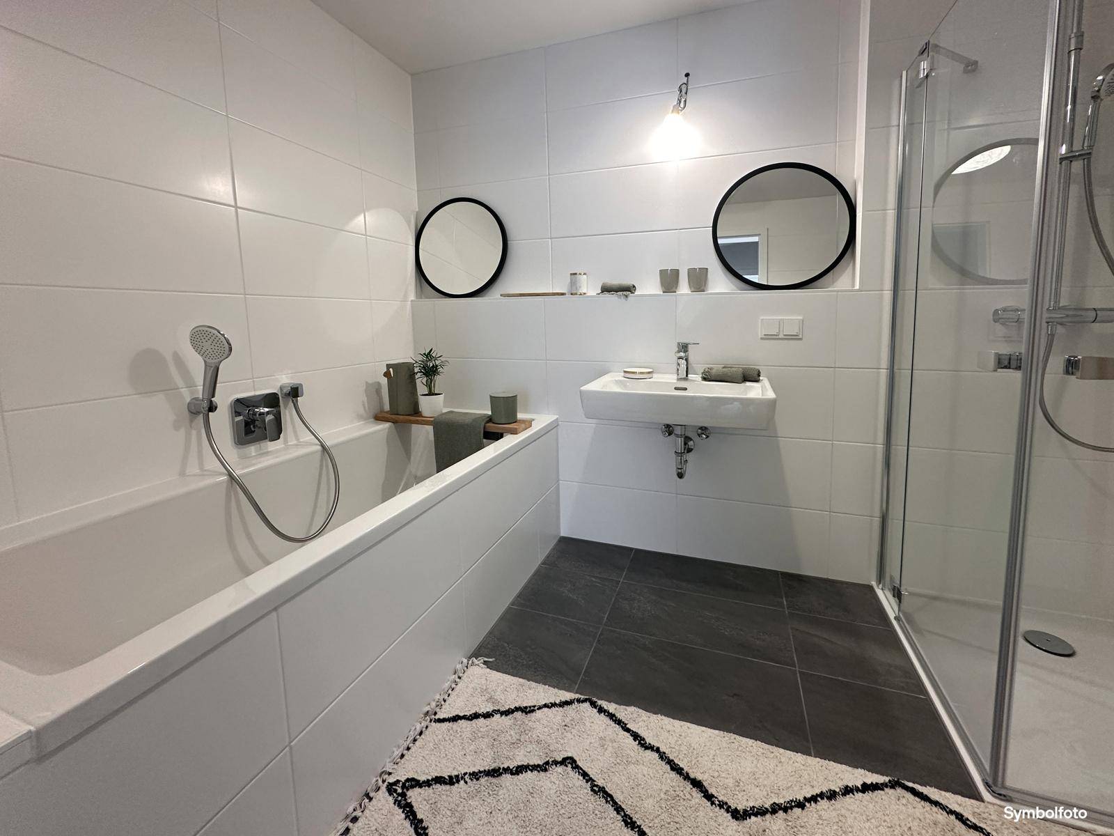 Modernes Badezimmer mit weißen Fliesen, Badewanne, Dusche und stilvollen runden Spiegeln.