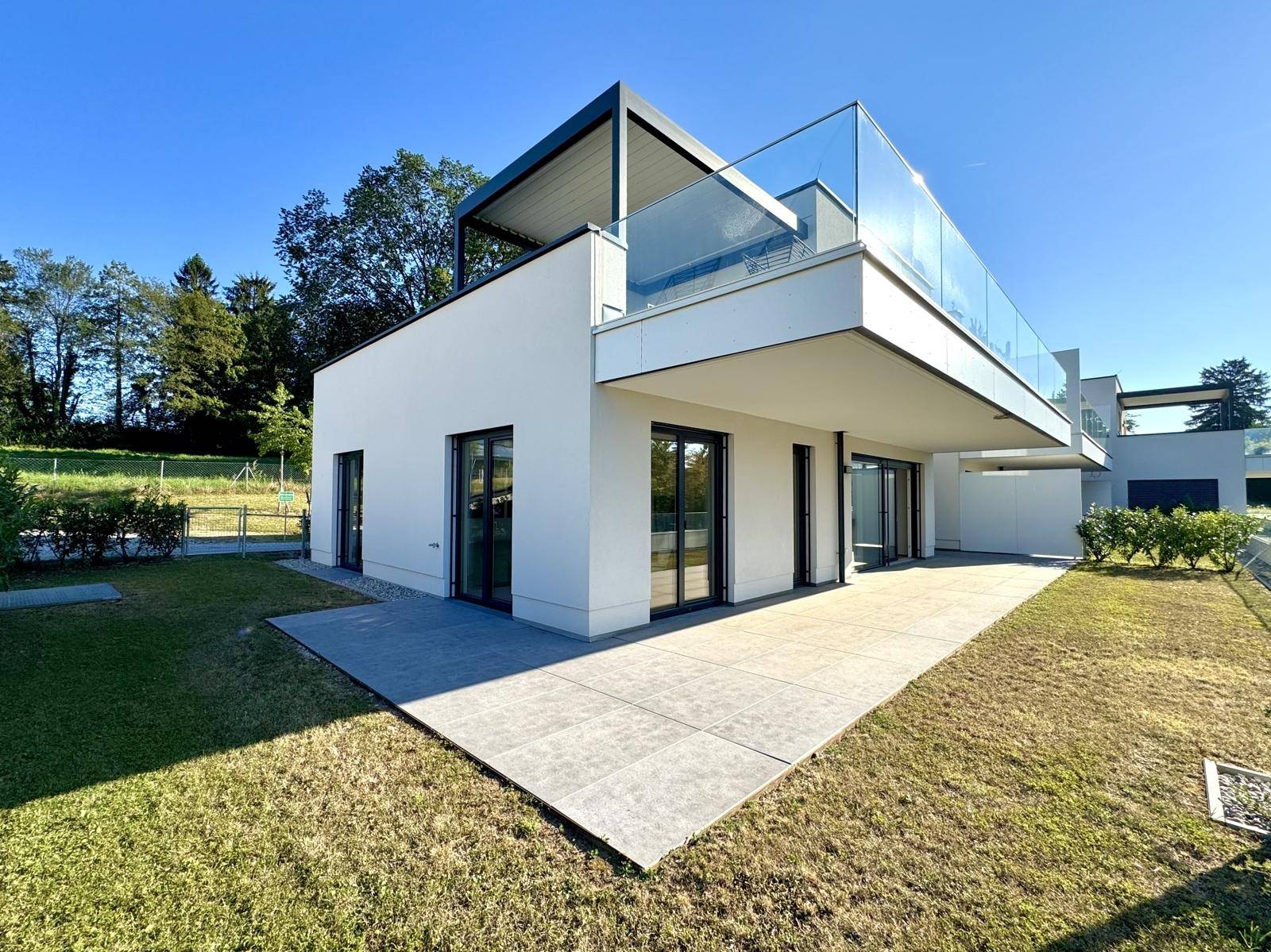 Großzügige Terrasse mit Fliesenboden und angrenzendem Rasenbereich an einem modernen Gebäude.