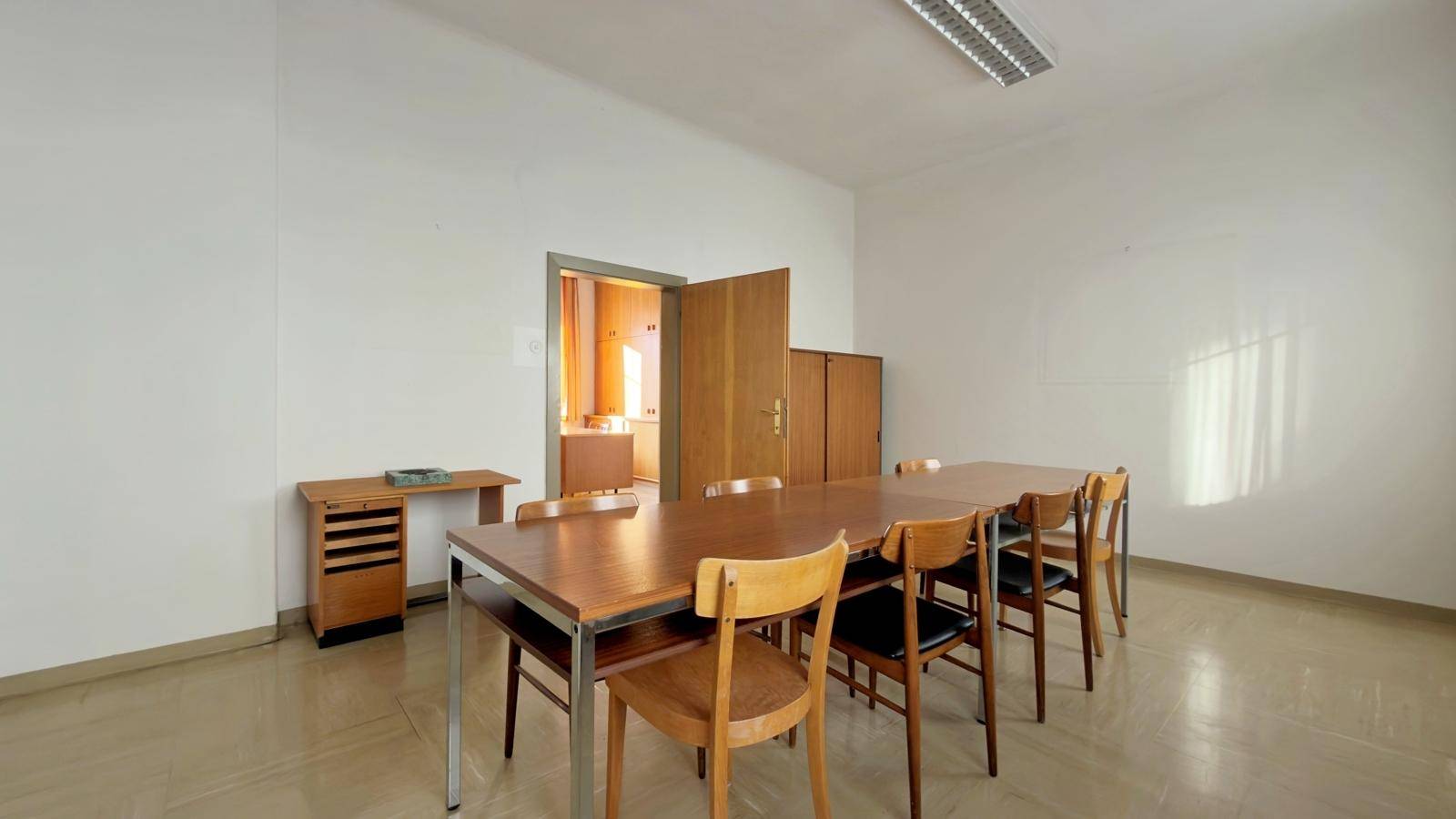 Konferenzraum mit langem Holztisch, mehreren Stühlen und hellem Bodenbelag, ideal für Besprechungen.