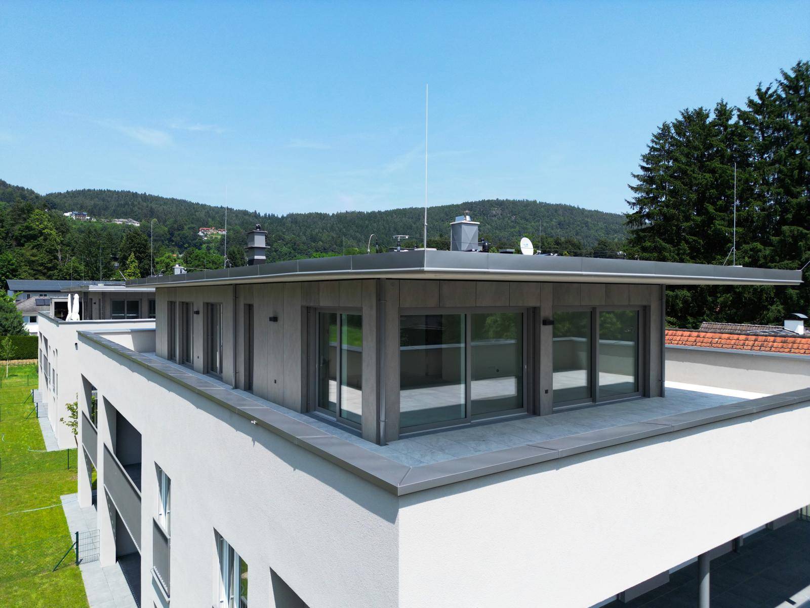 Dachbereich eines modernen Gebäudes mit großen Fenstern und flachem Dach unter blauem Himmel.
