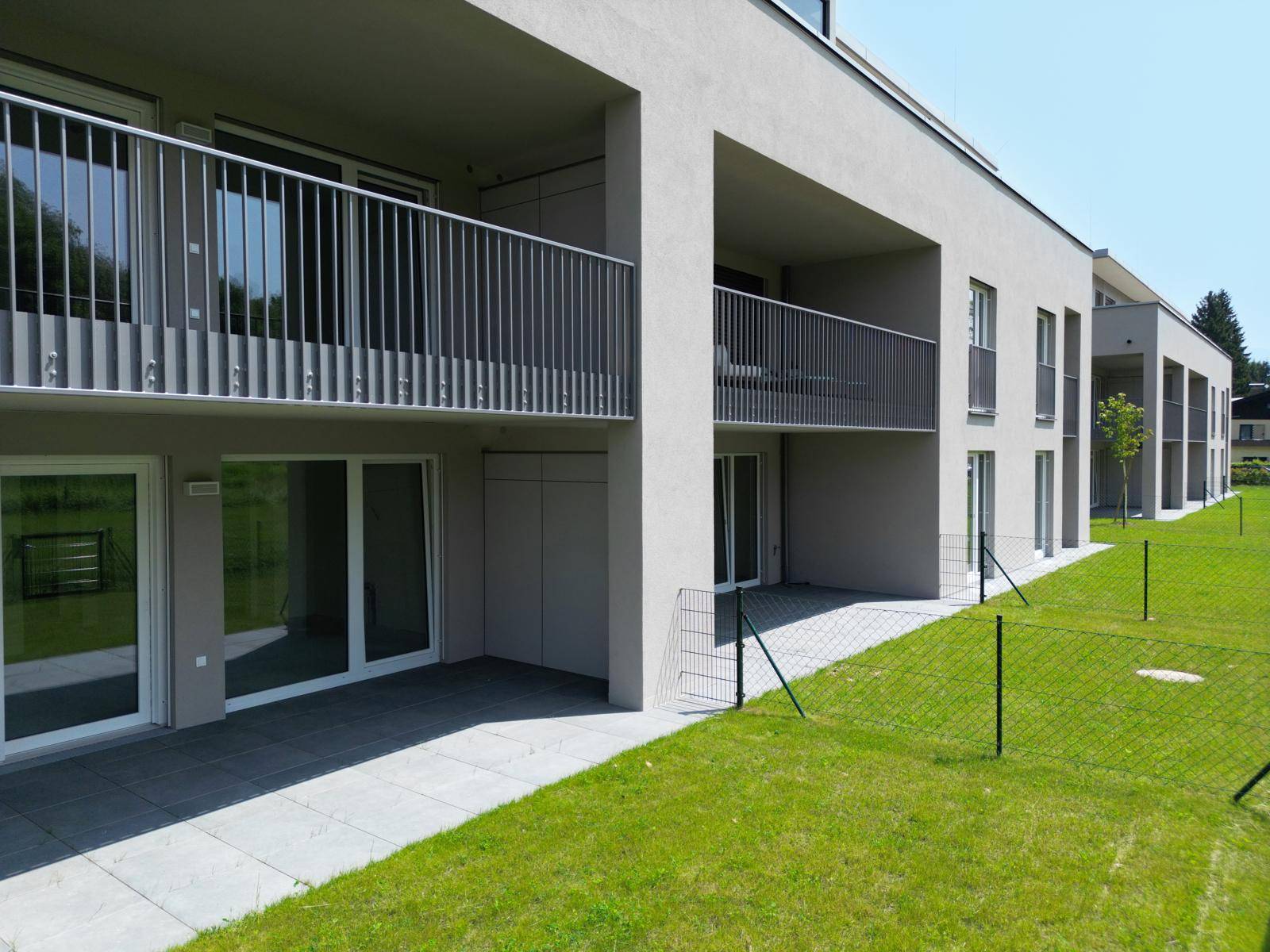 Nahaufnahme der Gebäudeseite mit mehreren Terrassen und Balkonen, umgeben von einer grünen Rasenfläche.