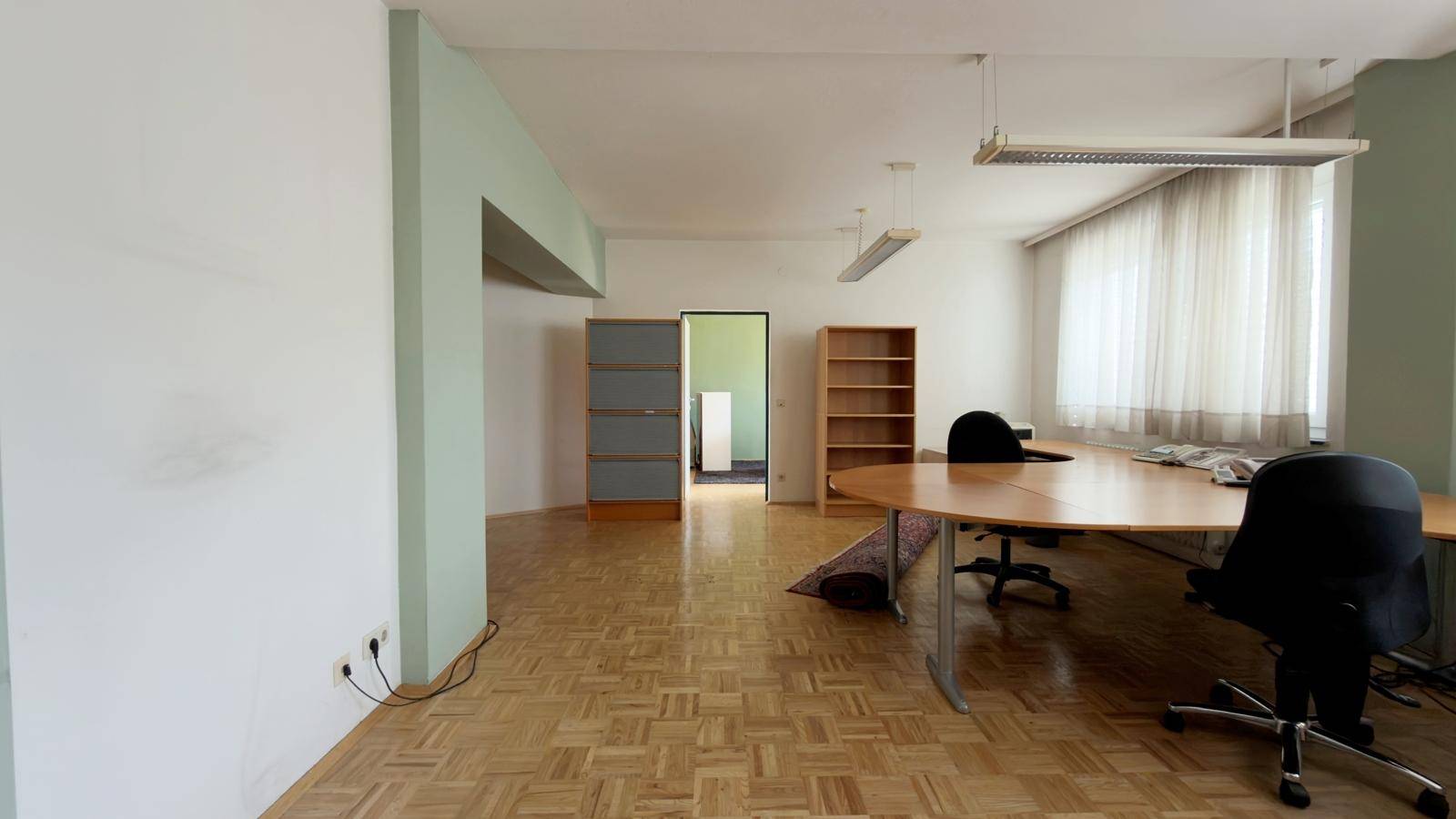 Heller Büroraum mit Fischgrätparkett und großen Fenstern, ideal für eine produktive Arbeitsumgebung.