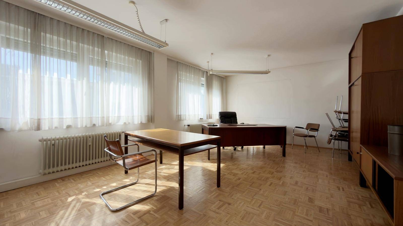 Geräumiges Büro mit Fischgrätparkett, großen Fenstern und viel Tageslicht, ideal für Arbeitsbereiche.