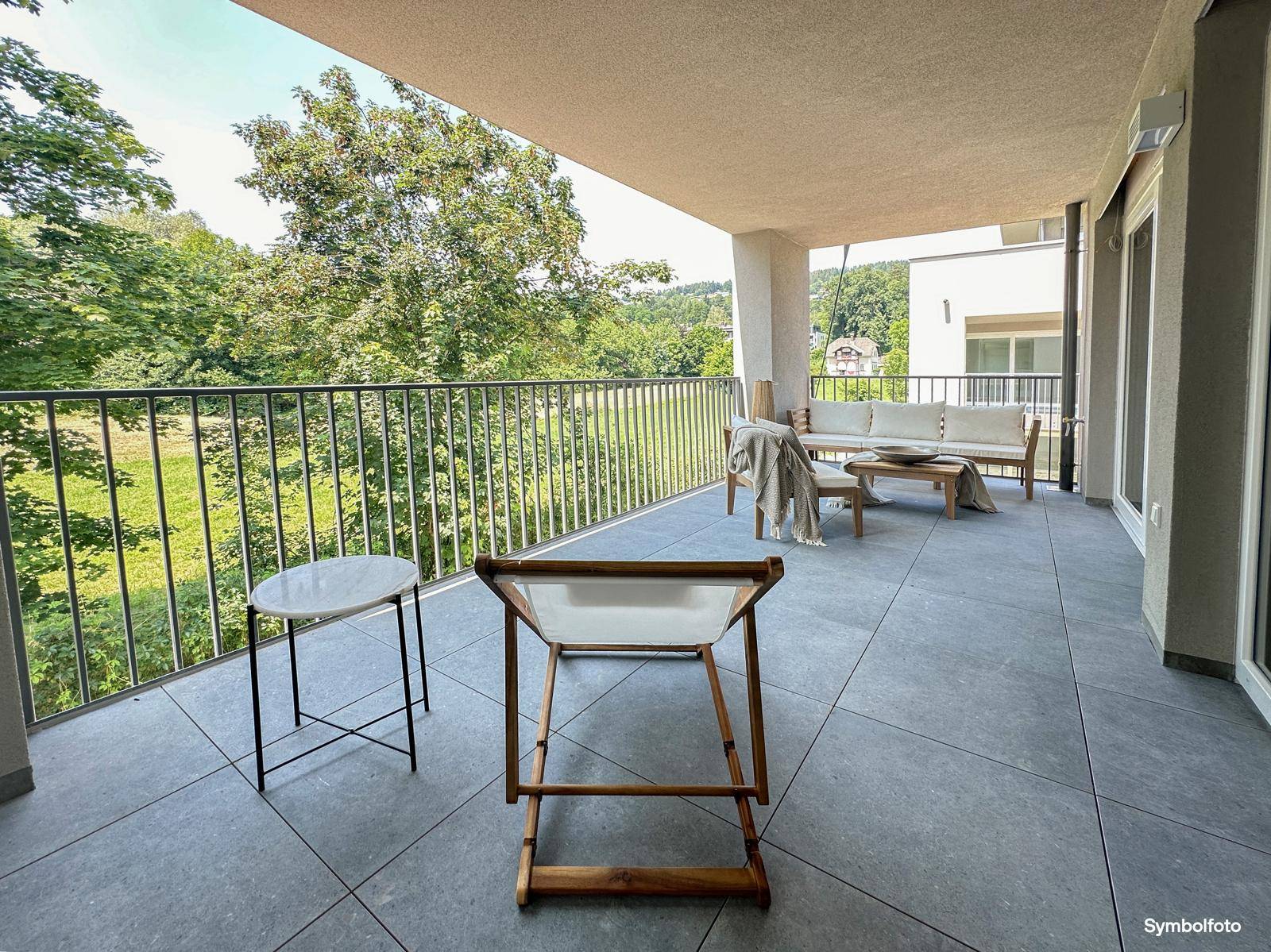 Langer Balkon mit Liegestuhl, Fliesenboden und einer ruhigen Aussicht ins Grüne.