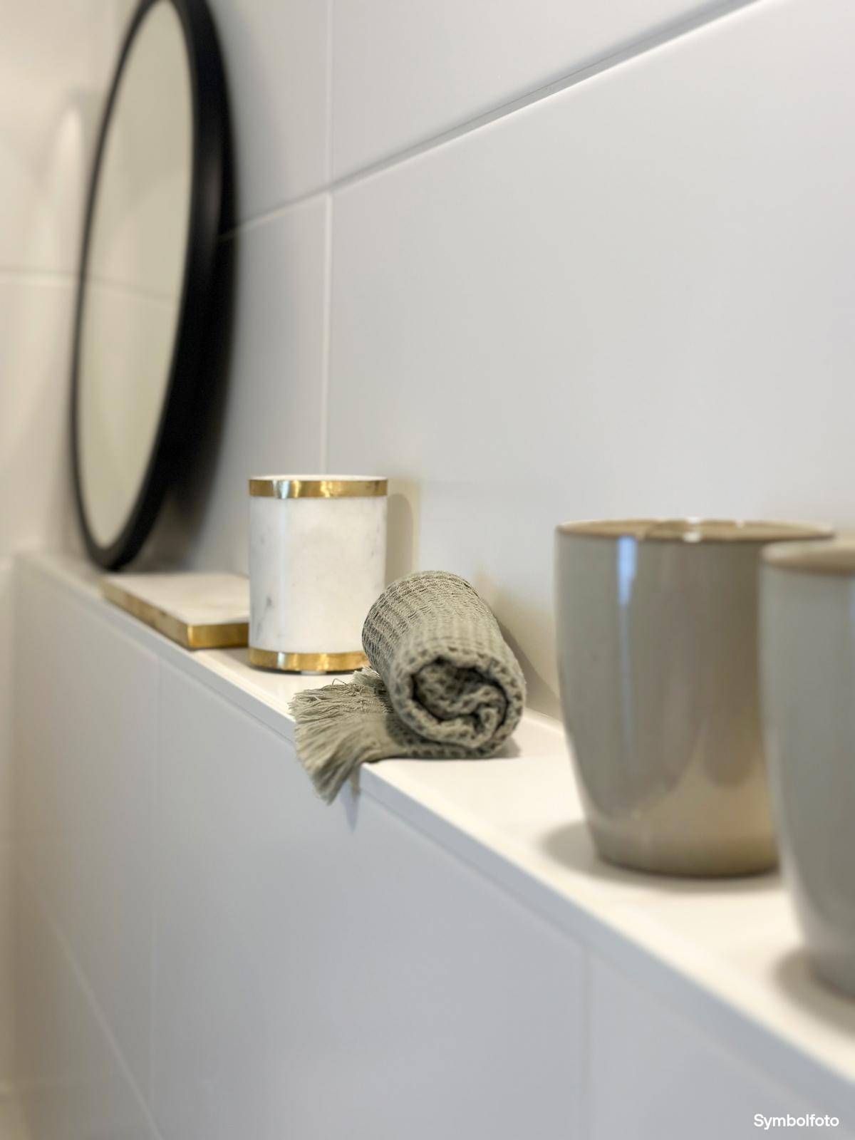 Dekorative Elemente auf einer Ablage im Badezimmer, darunter ein gerolltes Handtuch und Becher.