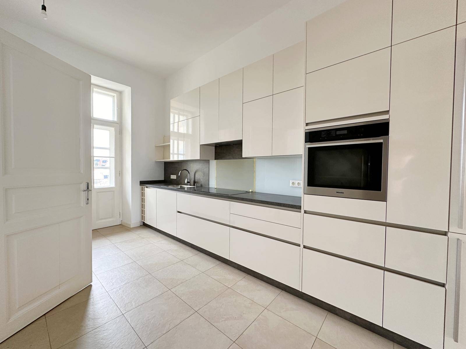 Moderne Einbauküche mit weißen Hochglanzfronten, dunkler Arbeitsplatte und integrierten Geräten.