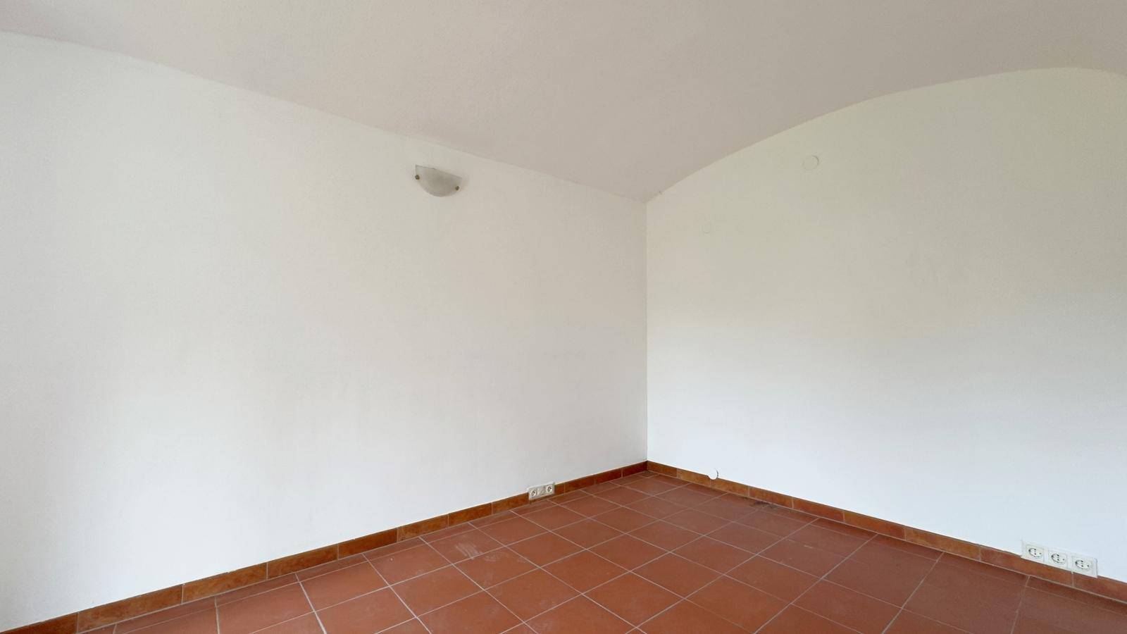 Leerer Raum mit weißen Wänden, Terrakottafliesen und einer sanften Gewölbedecke.