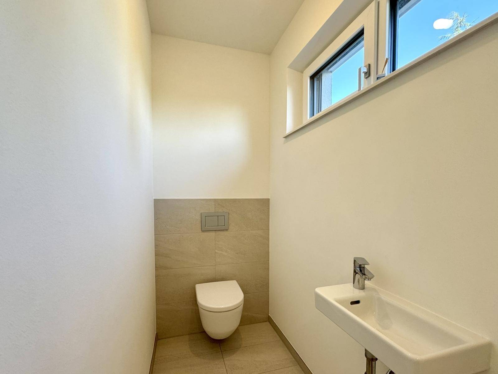 Modernes Gäste-WC mit Wand-WC, kleinem Waschbecken und Fenster für Tageslicht.