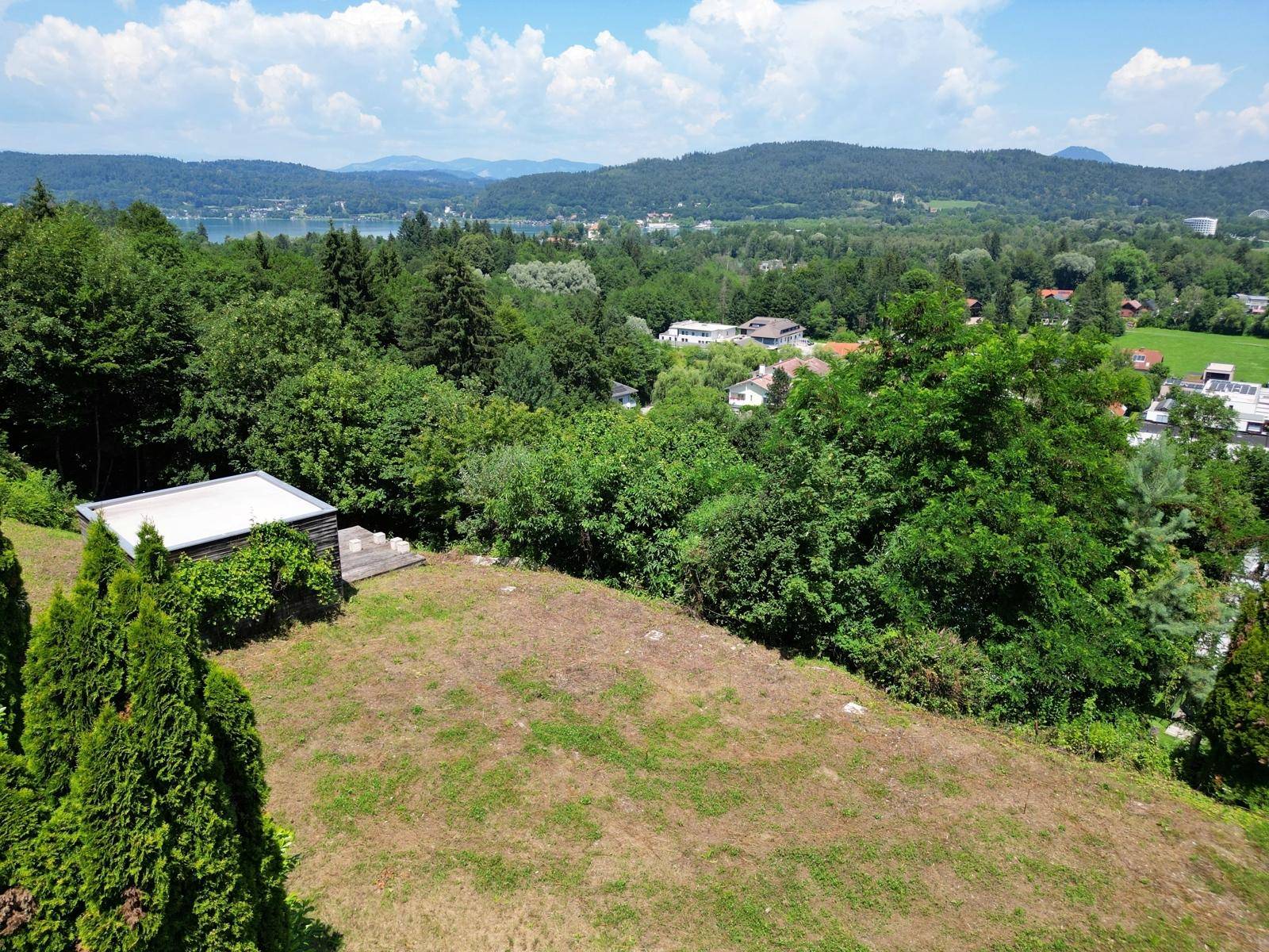 Luftaufnahme eines Grundstücks mit kleinem Schuppen, umgeben von Bäumen und mit Seeblick.