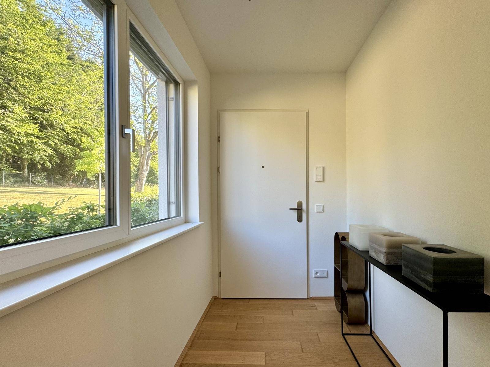 Heller Flur mit Eichenparkett, großem Fenster und weißer Eingangstür, einladend gestaltet.