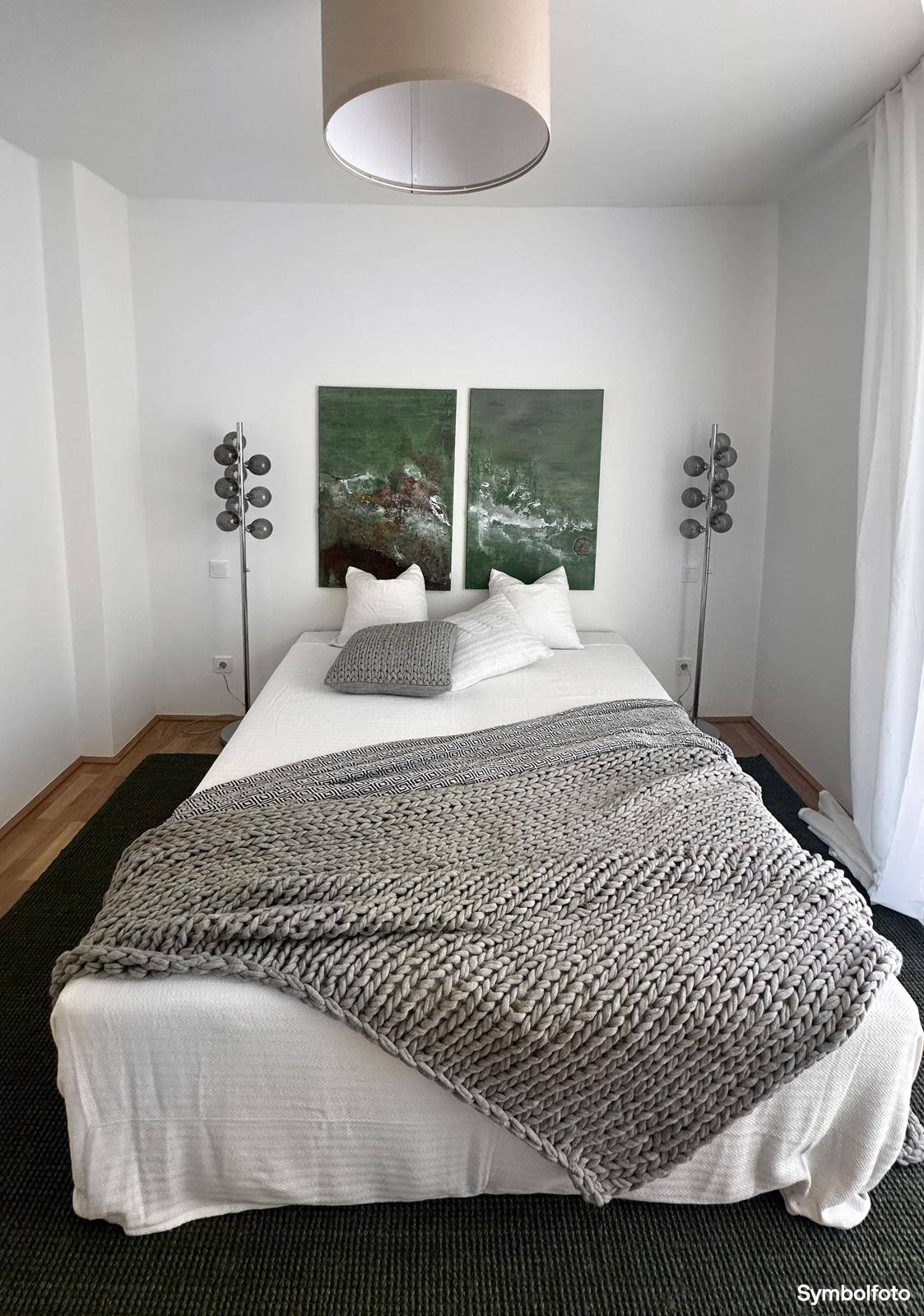 Gemütliches Schlafzimmer mit modernem Bett, grünen Kunstwerken und stilvollen Stehlampen.