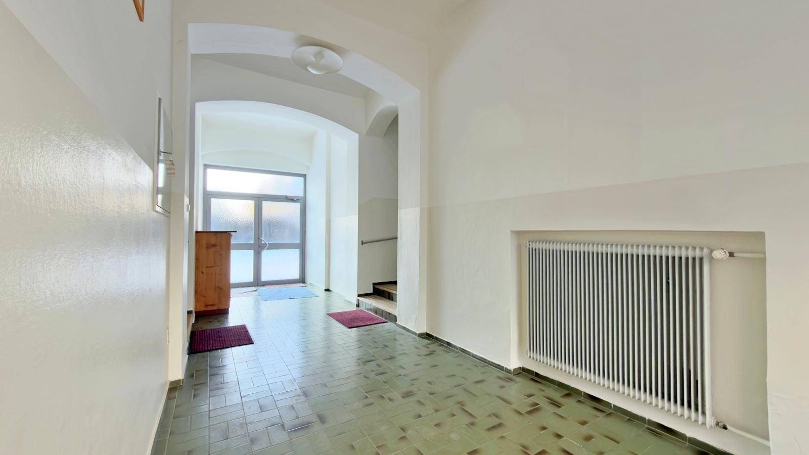 Heller Eingangsbereich mit gefliestem Boden, Heizkörper und Blick zur Eingangstür und Treppe.